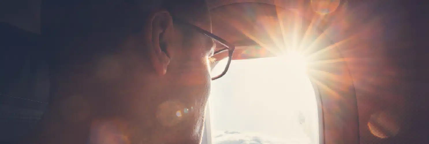 A man looking out of an airplane window with sunshine