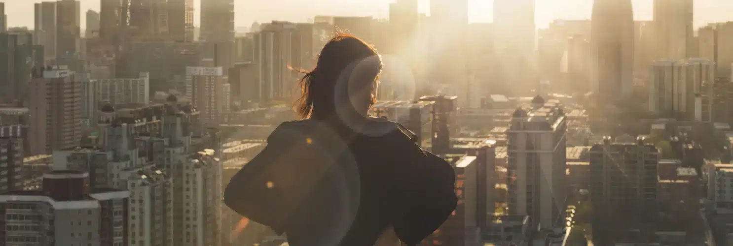 A woman on a rooftop gazes at the cityscape below her, captivated by the urban beauty.