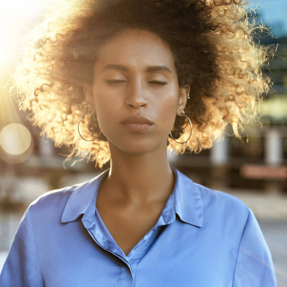 A woman with an afro hairstyle gazes at the sun, captivated by its radiant beauty.