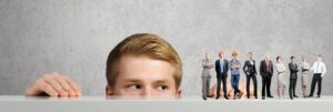 A man peeks from behind a group of business professionals, representing Market IQ from Textkernel by Bullhorn.